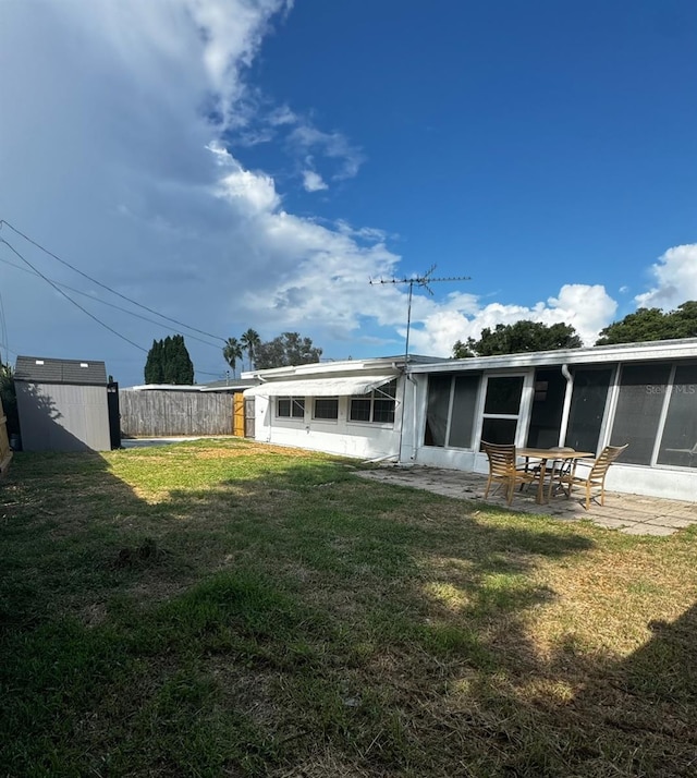 rear view of property with a lawn, a sunroom, and a storage shed