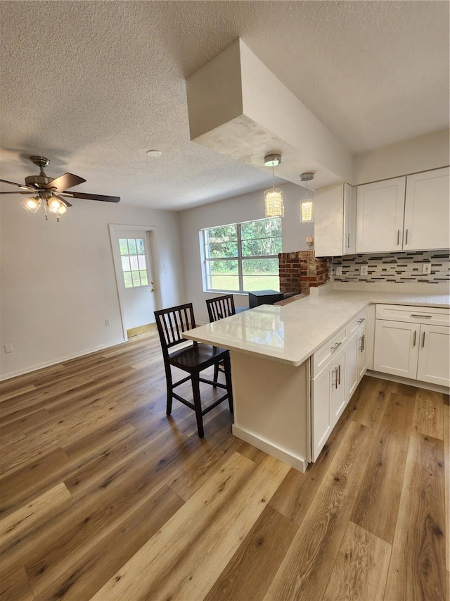 kitchen with white cabinetry, kitchen peninsula, light hardwood / wood-style floors, and hanging light fixtures