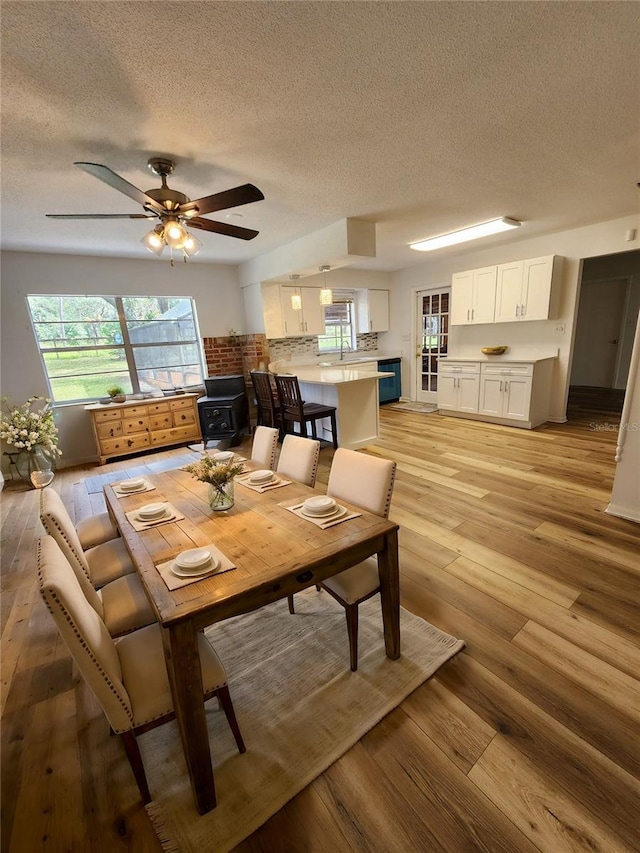 dining room with sink, light wood-type flooring, a textured ceiling, and ceiling fan