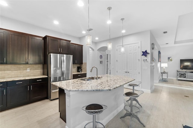 kitchen featuring pendant lighting, a kitchen breakfast bar, sink, stainless steel fridge, and an island with sink