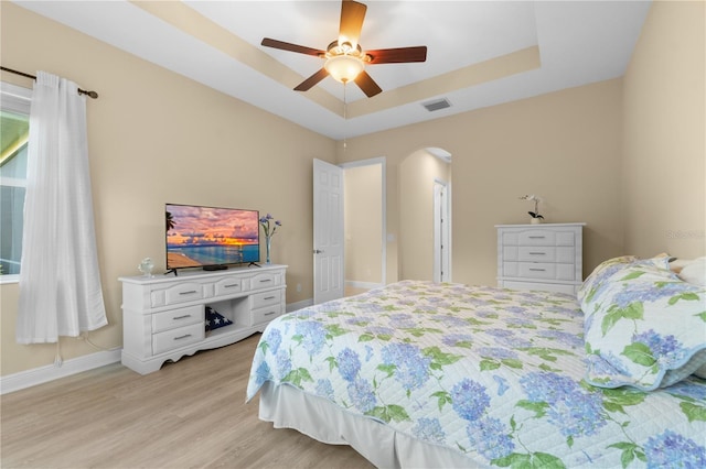 bedroom with a raised ceiling, ceiling fan, and light hardwood / wood-style flooring