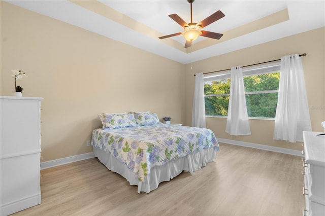 bedroom featuring light wood-type flooring, a tray ceiling, and ceiling fan