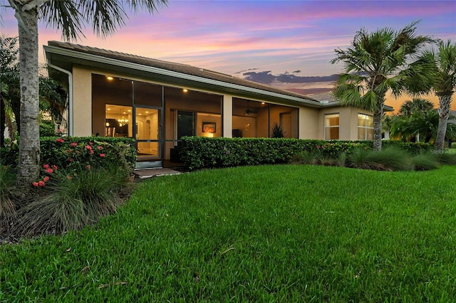 back house at dusk featuring a lawn