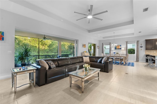 living room with ceiling fan with notable chandelier, a tray ceiling, and light tile patterned flooring