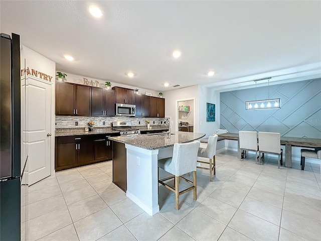 kitchen featuring dark brown cabinets, an island with sink, a kitchen breakfast bar, dark stone counters, and stainless steel appliances