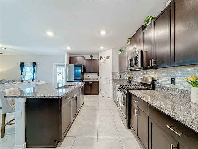 kitchen with appliances with stainless steel finishes, sink, a kitchen breakfast bar, light stone counters, and a kitchen island with sink