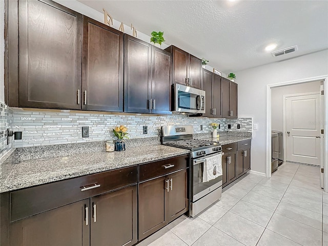 kitchen featuring decorative backsplash, light tile patterned floors, appliances with stainless steel finishes, dark brown cabinetry, and light stone counters