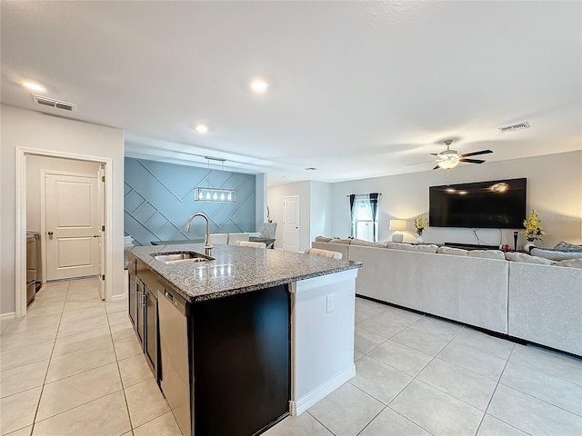 kitchen with an island with sink, sink, light tile patterned floors, stainless steel dishwasher, and light stone counters