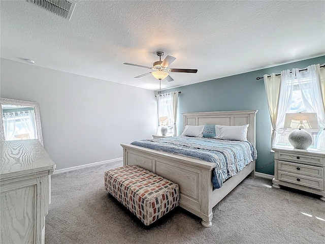 bedroom with a textured ceiling, ceiling fan, multiple windows, and light colored carpet