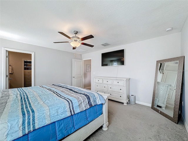 carpeted bedroom with a closet, ceiling fan, a textured ceiling, and a walk in closet