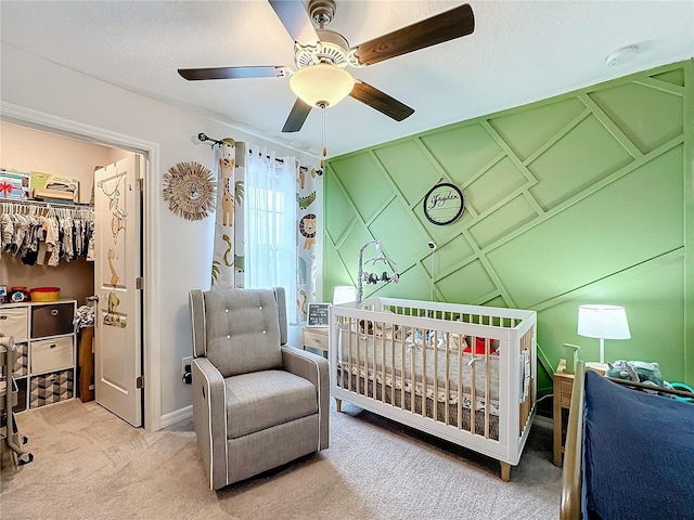 bedroom with a textured ceiling, carpet flooring, a crib, and ceiling fan