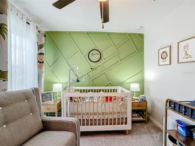 bedroom with a nursery area, carpet floors, and ceiling fan