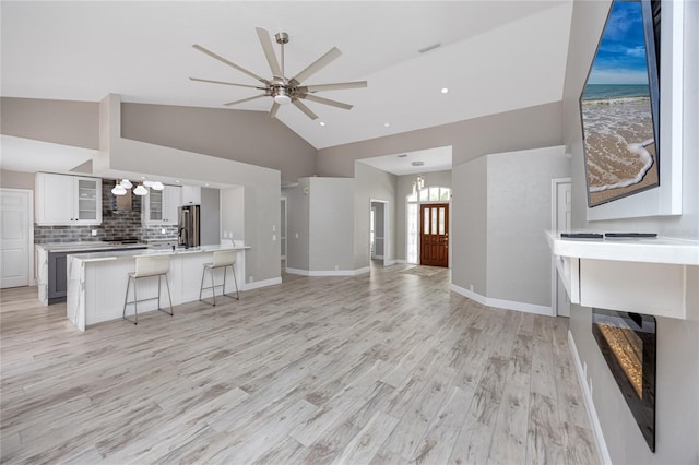 unfurnished living room with ceiling fan with notable chandelier, a multi sided fireplace, light hardwood / wood-style floors, and high vaulted ceiling