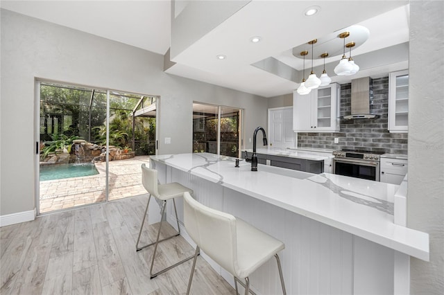 kitchen featuring high end range, wall chimney exhaust hood, white cabinetry, a breakfast bar, and light hardwood / wood-style floors