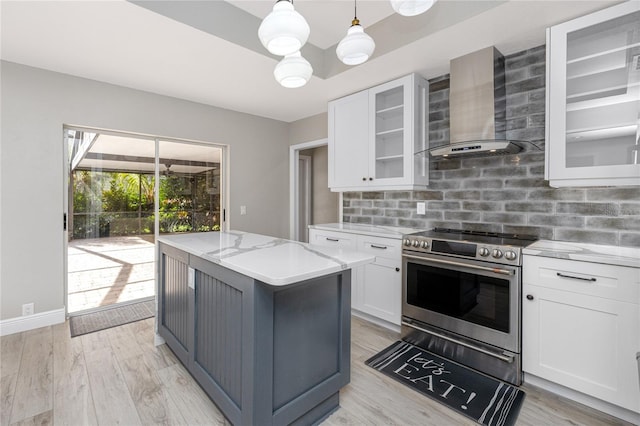 kitchen featuring light stone counters, a center island, white cabinetry, wall chimney exhaust hood, and stainless steel range with electric stovetop