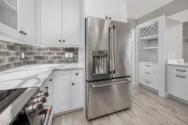 kitchen featuring white cabinetry, light stone counters, tasteful backsplash, stainless steel appliances, and light wood-type flooring