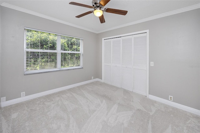 unfurnished bedroom featuring ceiling fan, a textured ceiling, a closet, light carpet, and crown molding