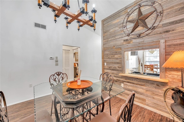 dining room with hardwood / wood-style flooring, a notable chandelier, beam ceiling, high vaulted ceiling, and wooden walls