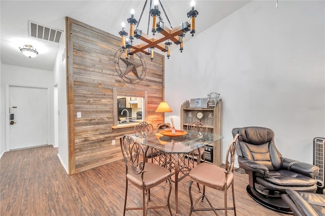 dining room with an inviting chandelier, hardwood / wood-style flooring, wood walls, and a high ceiling