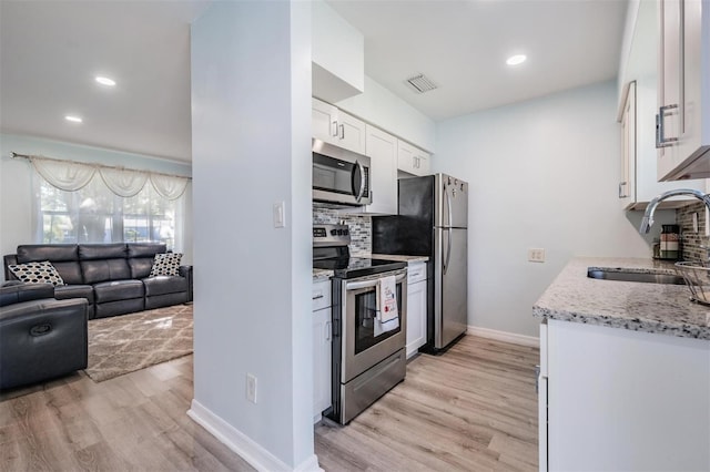 kitchen with sink, white cabinetry, stainless steel appliances, light stone countertops, and light hardwood / wood-style floors