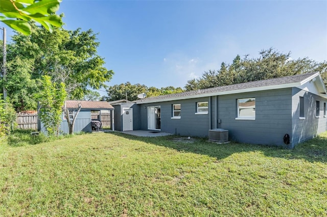 rear view of property with a lawn, central AC, and a storage unit