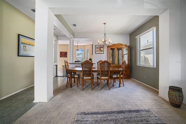 dining area featuring an inviting chandelier, dark colored carpet, a textured ceiling, and ornate columns