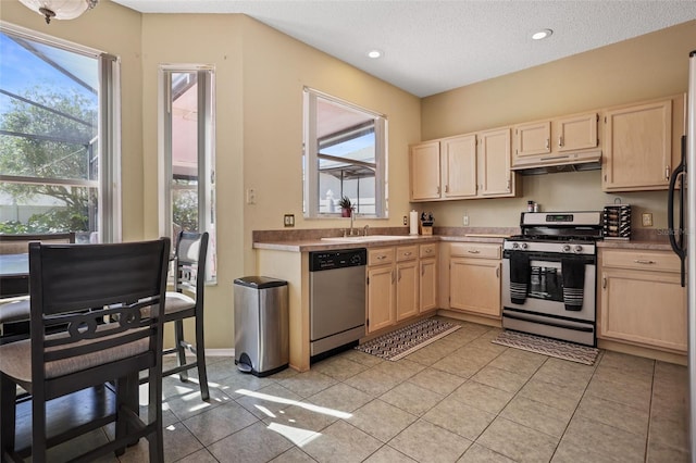 kitchen with a textured ceiling, light brown cabinets, light tile patterned floors, and stainless steel appliances