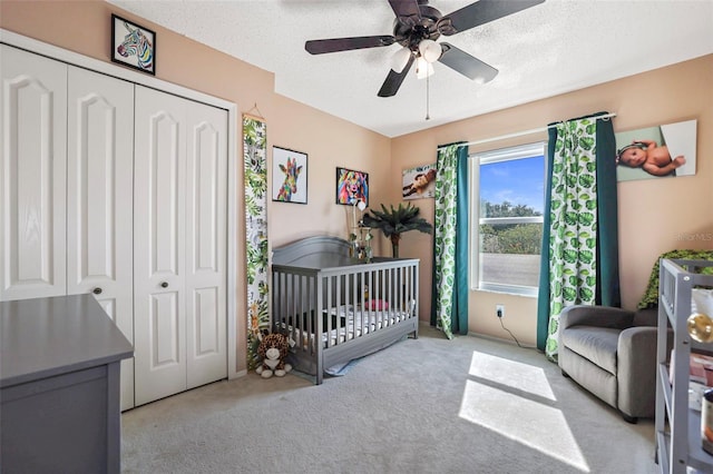 carpeted bedroom featuring a closet, ceiling fan, a nursery area, and a textured ceiling