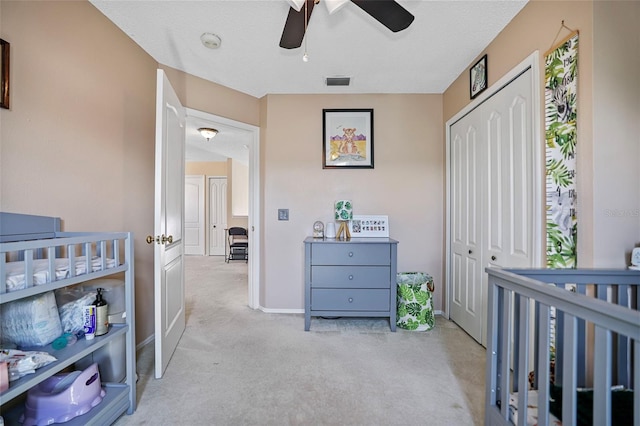 carpeted bedroom with ceiling fan, a textured ceiling, a closet, and a crib