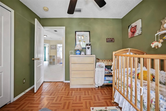 unfurnished bedroom with ceiling fan, a nursery area, a textured ceiling, and light parquet floors