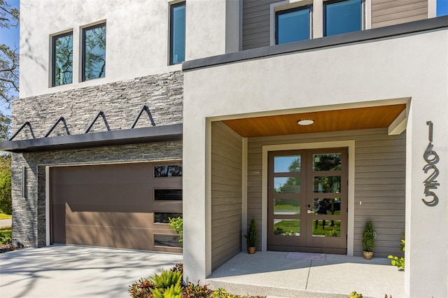 property entrance featuring a garage, french doors, stone siding, and stucco siding
