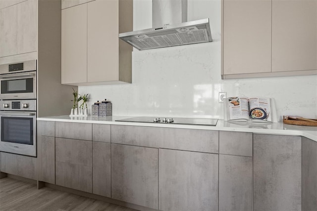 kitchen featuring wall chimney exhaust hood, double oven, light hardwood / wood-style flooring, and black electric stovetop