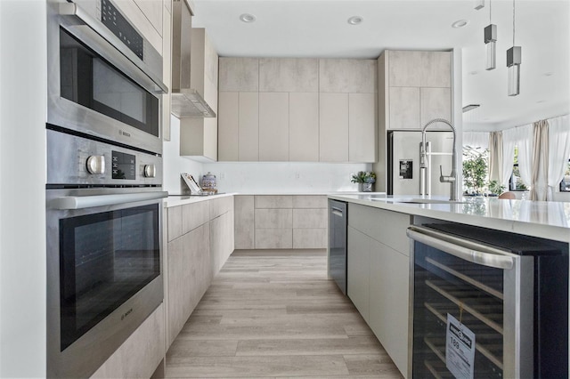 kitchen with high end fridge, wall chimney exhaust hood, hanging light fixtures, beverage cooler, and light hardwood / wood-style floors