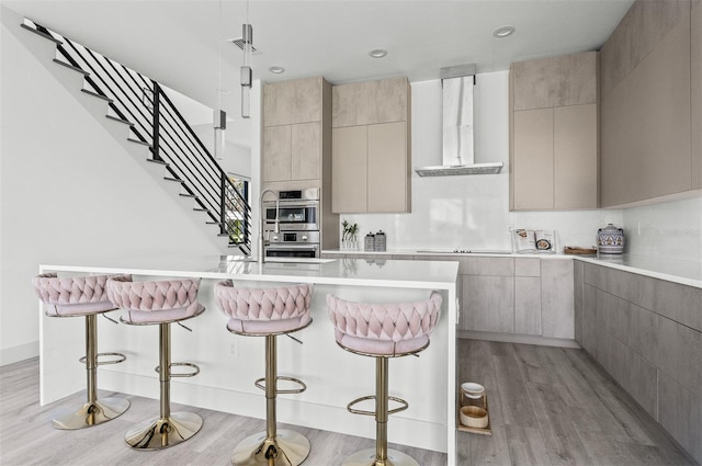 kitchen with a kitchen island, double oven, a kitchen breakfast bar, light hardwood / wood-style floors, and extractor fan