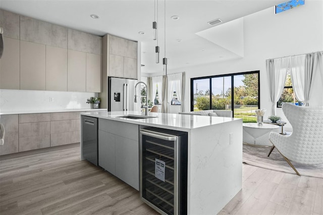 kitchen with gray cabinetry, wine cooler, a center island with sink, pendant lighting, and light hardwood / wood-style floors