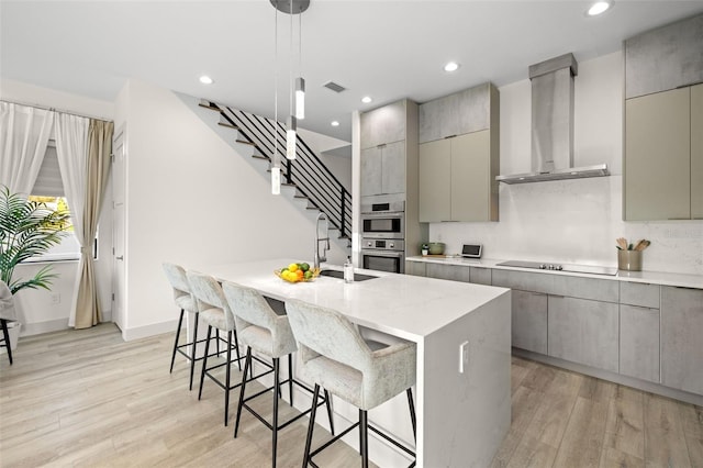 kitchen featuring gray cabinets, wall chimney range hood, and light wood-type flooring