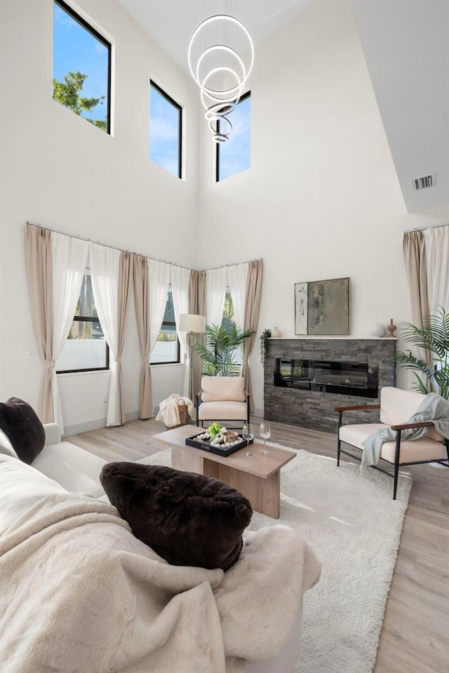 living room featuring wood finished floors, a chandelier, a towering ceiling, a fireplace, and visible vents
