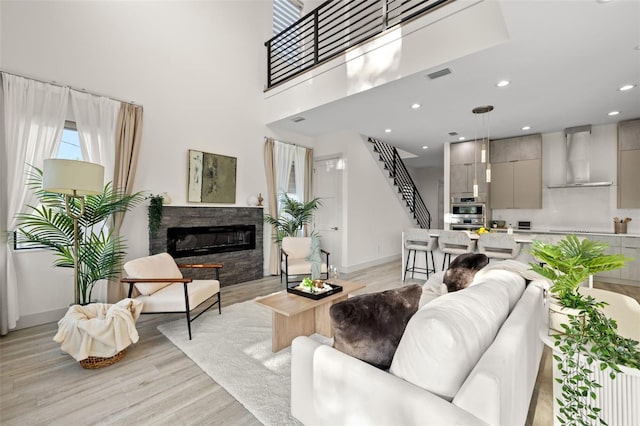 living room with a glass covered fireplace, light wood-style flooring, stairs, and baseboards