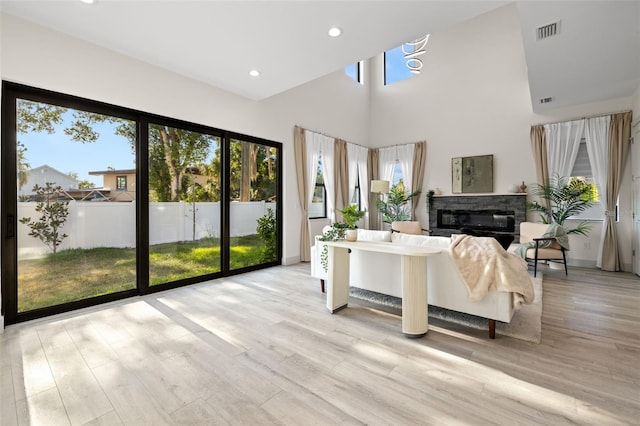 living room featuring a healthy amount of sunlight, a glass covered fireplace, a towering ceiling, and visible vents