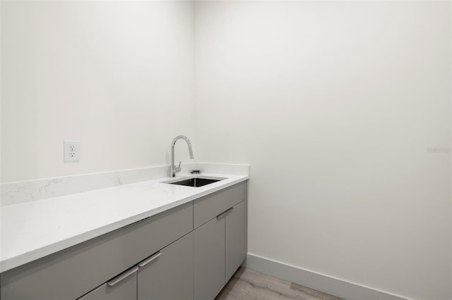 laundry area featuring light wood-style floors, baseboards, and a sink