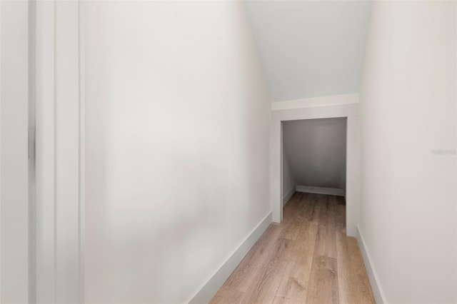 hallway featuring lofted ceiling, light wood finished floors, and baseboards