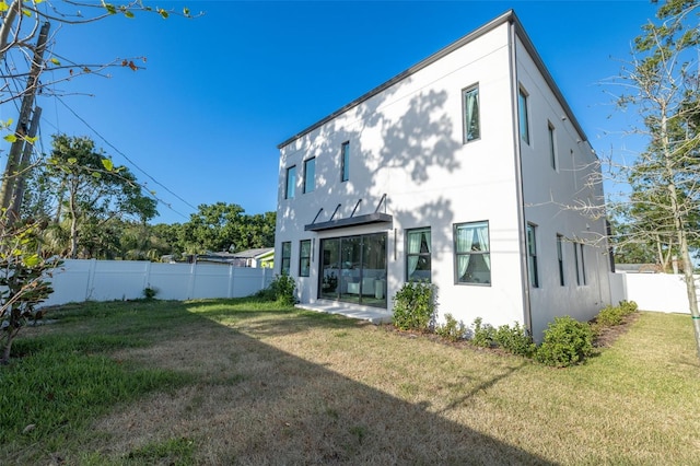 rear view of house featuring stucco siding, a yard, and a fenced backyard