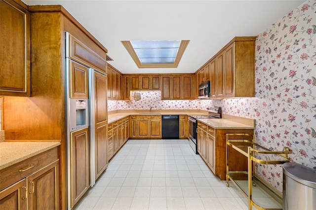 kitchen featuring stainless steel appliances, light stone counters, a skylight, and sink