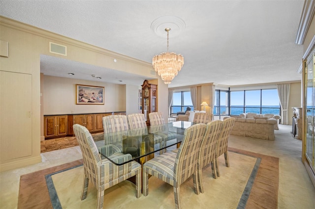 carpeted dining room with a textured ceiling, a water view, ornamental molding, and an inviting chandelier