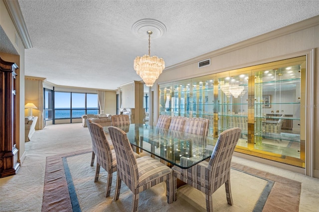 carpeted dining area with a textured ceiling, a water view, ornamental molding, and an inviting chandelier