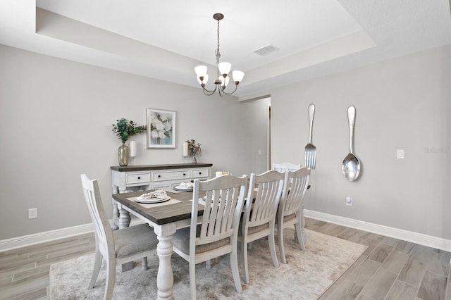 dining area featuring a notable chandelier, a raised ceiling, and light hardwood / wood-style floors