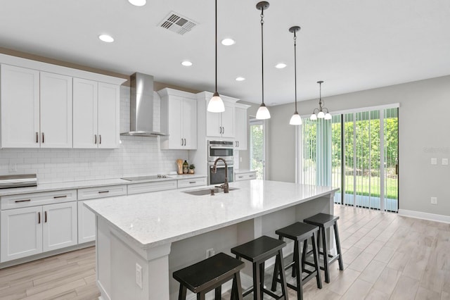 kitchen featuring an island with sink, pendant lighting, wall chimney range hood, and black electric cooktop