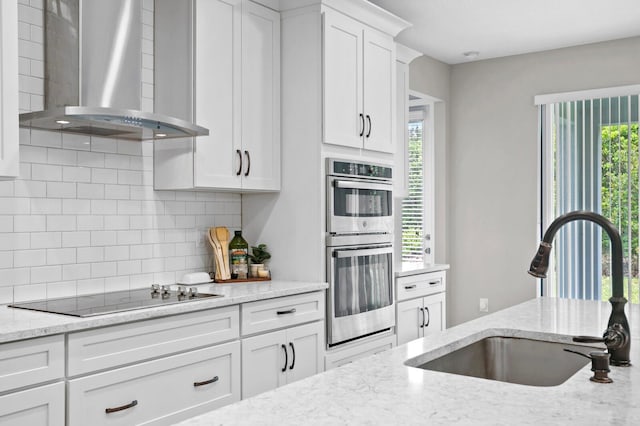 kitchen featuring white cabinets, sink, wall chimney exhaust hood, double oven, and black electric stovetop