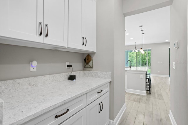 kitchen featuring light wood-type flooring, sink, white cabinetry, decorative light fixtures, and light stone countertops