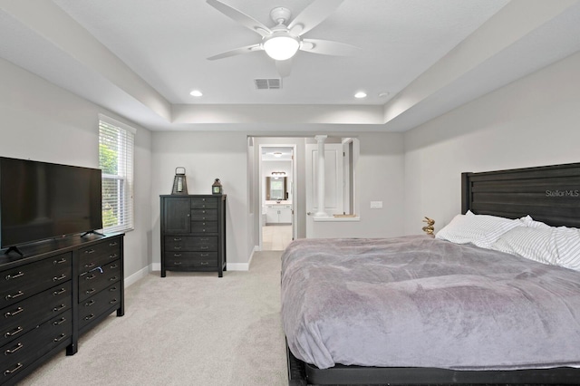 carpeted bedroom featuring a tray ceiling, ceiling fan, and ensuite bath